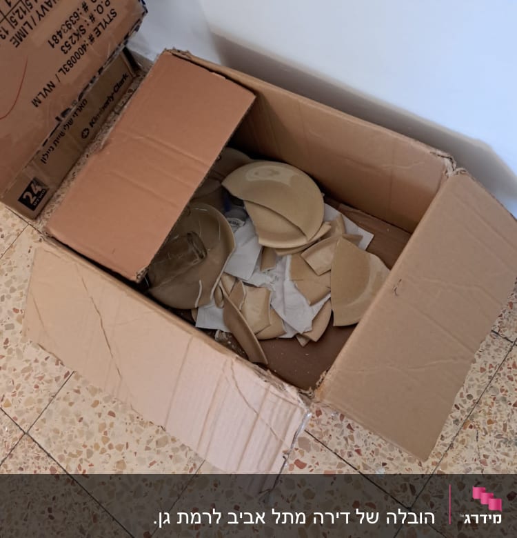 קרטון פתוח עם כלים שבורים על רצפה